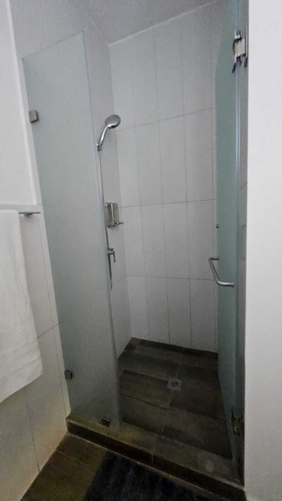 A small, enclosed shower area with a tiled floor and walls, a showerhead, and a door with a handle.