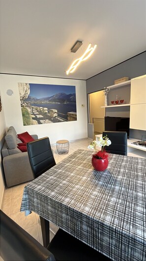 A modern living room with a large window, a dining table, and a sofa. - Apartment with a 150-square-meter Private Terrace and Breathtaking Lake Views (Trentino-Alto Adige)