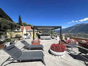 A rooftop terrace with lounge chairs, a covered seating area, and potted plants. - Apartment with a 150-square-meter Private Terrace and Breathtaking Lake Views (Trentino-Alto Adige)