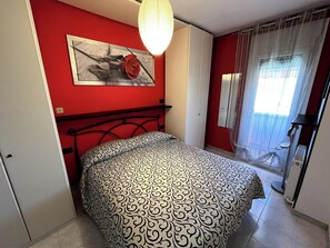 A bedroom with a bed, a red wall, a painting, and a window with curtains. - Apartment with a 150-square-meter Private Terrace and Breathtaking Lake Views (Trentino-Alto Adige)