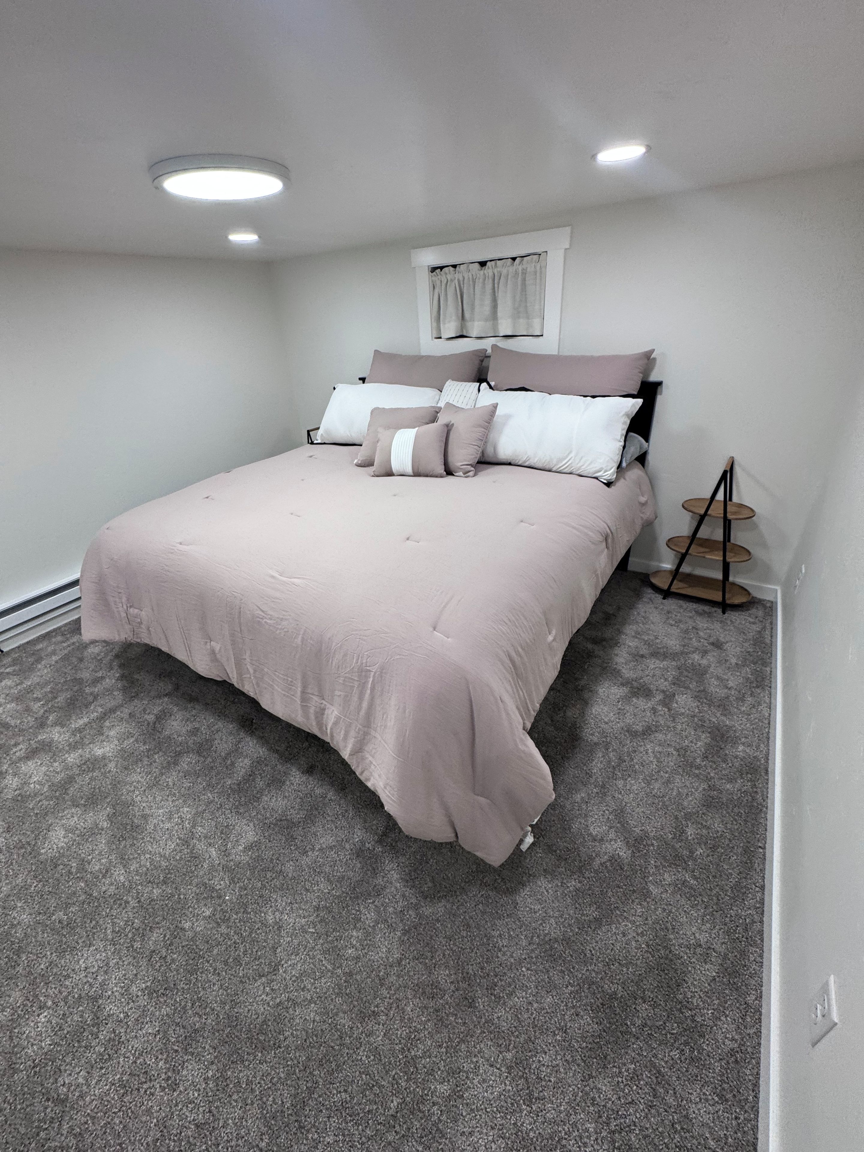 Una camera da letto con un letto, una finestra con tende, un tavolino di legno e un pavimento rivestito di moquette.