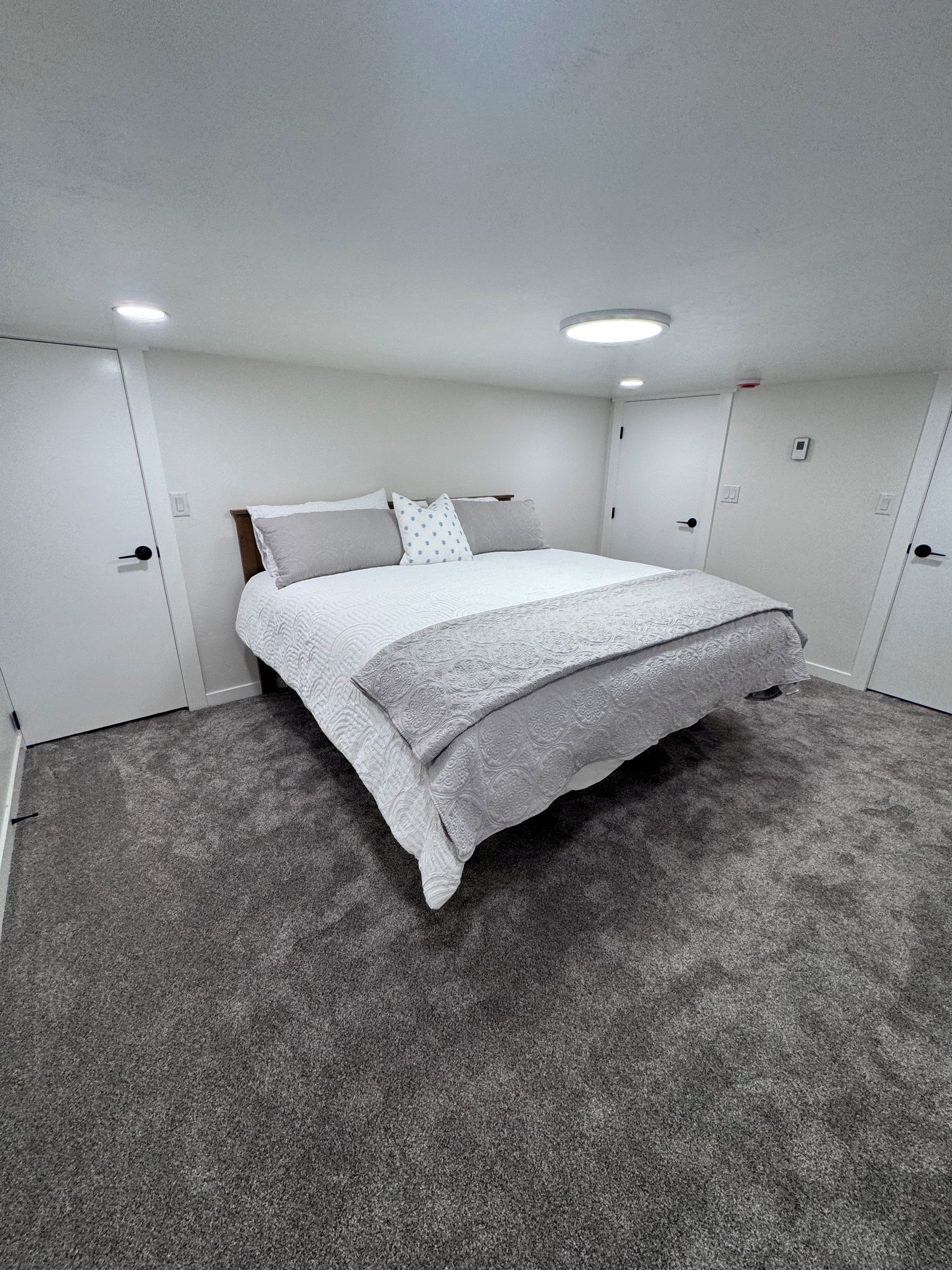 Ein Schlafzimmer mit einem Bett, Teppichboden, weißen Wänden und einer Deckenleuchte.