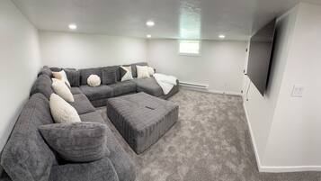 Uma sala de estar moderna com um sofá seccional, um banquinho e uma TV de tela plana na parede.