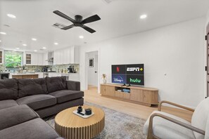 Una sala moderna con un sofá modular, una mesa de centro y un televisor mostrando logotipos de servicios de transmisión.