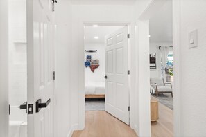 Un pasillo con puertas blancas que dan a una habitación con piso de madera y una silla blanca.