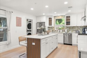 A modern kitchen with white cabinetry, a central island, and a built-in dishwasher. - Chef`s Kitchen + Fire Pit Patio | E Austin Bungalow Mins to Local Favs & Lady Bird (Austin)