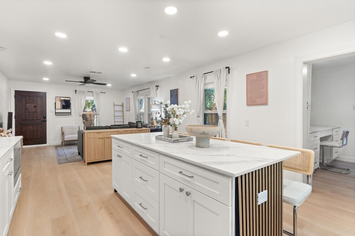 A modern kitchen with white cabinetry, a central island, and a dining area with a white chair.