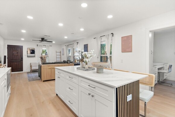 A modern kitchen with white cabinetry, a central island, and a dining area with a white chair.