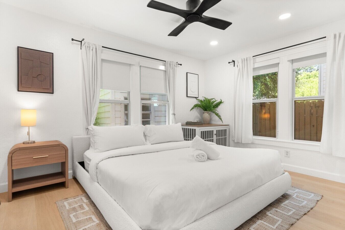 A bedroom with a bed, bedside table, lamp, window, and ceiling fan.