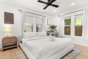 A bedroom with a bed, bedside table, lamp, window, and ceiling fan.