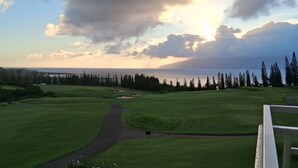 Campo de golf con cielo despejado, un sendero que lleva al tee y una masa de agua al fondo.