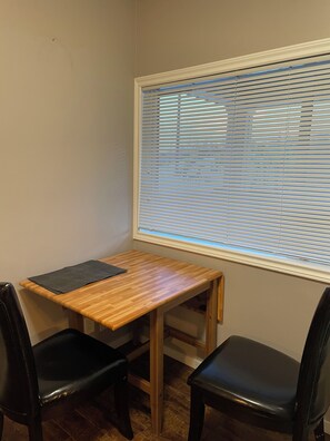 Een kleine kamer met een houten bureau, twee zwarte stoelen en een raam met jaloezieën.