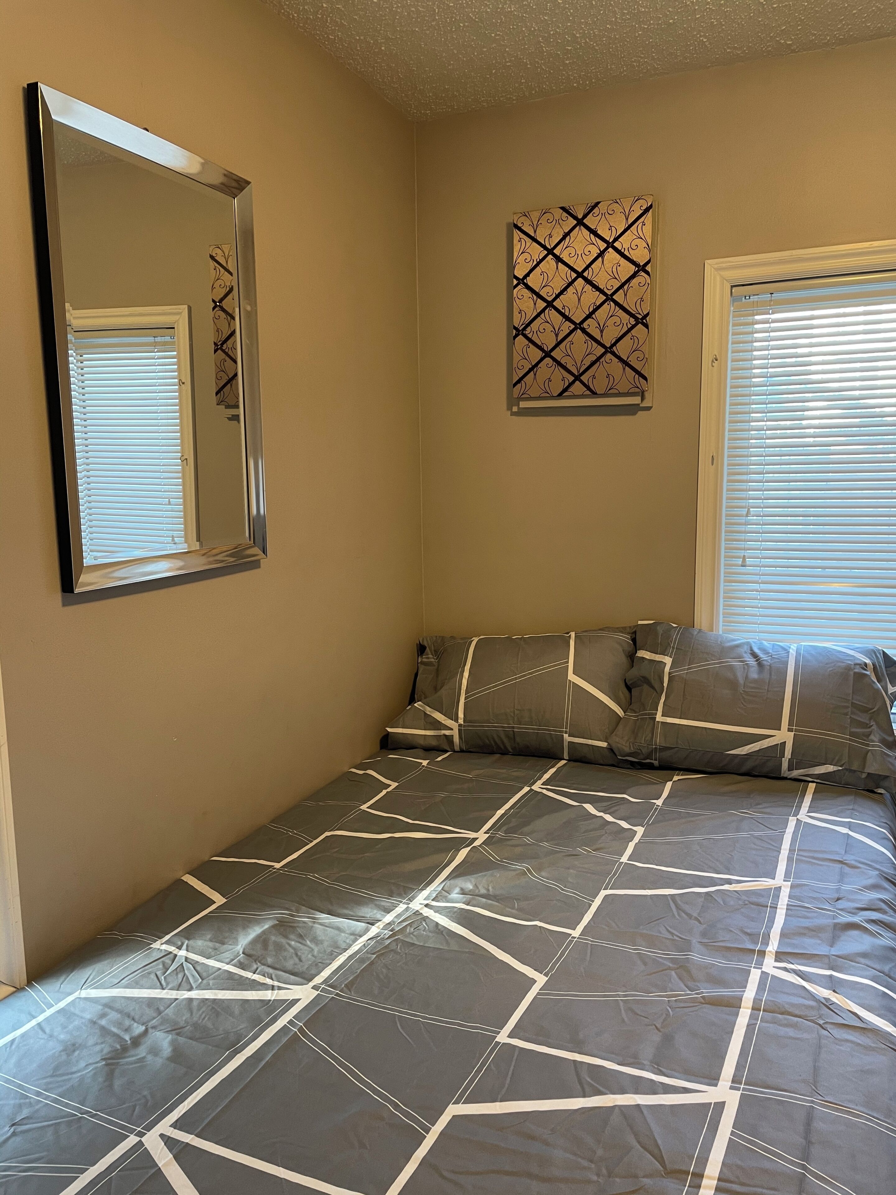 A bedroom with a bed, a large mirror, a decorative wall piece, and a window with blinds.