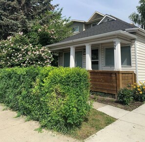 Een gelijkvloers huis met een veranda, een houten hek en een verzorgde tuin.