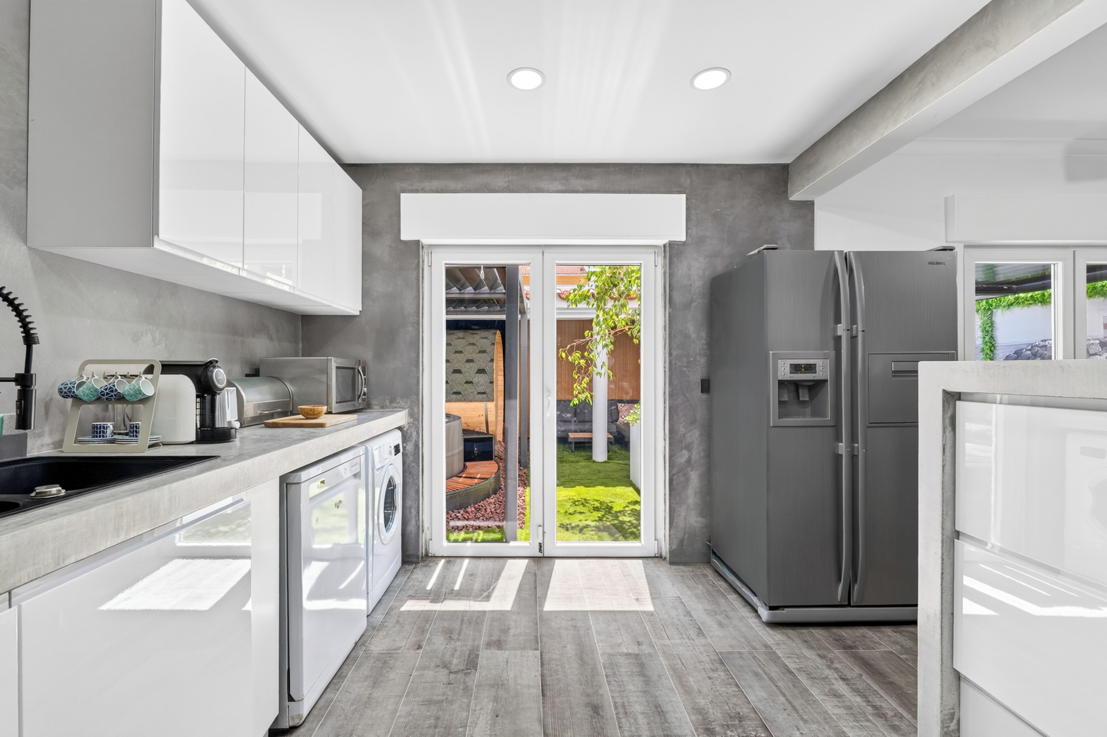 A modern kitchen with white cabinets, a built-in oven, a refrigerator, and a coffee machine.