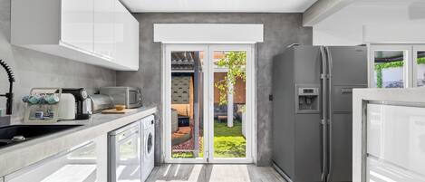 A modern kitchen with white cabinets, a built-in oven, a refrigerator, and a coffee machine.