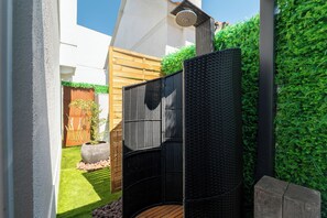 Um espaço moderno ao ar livre com estrutura metálica preta, deck de madeira e parede verde.
