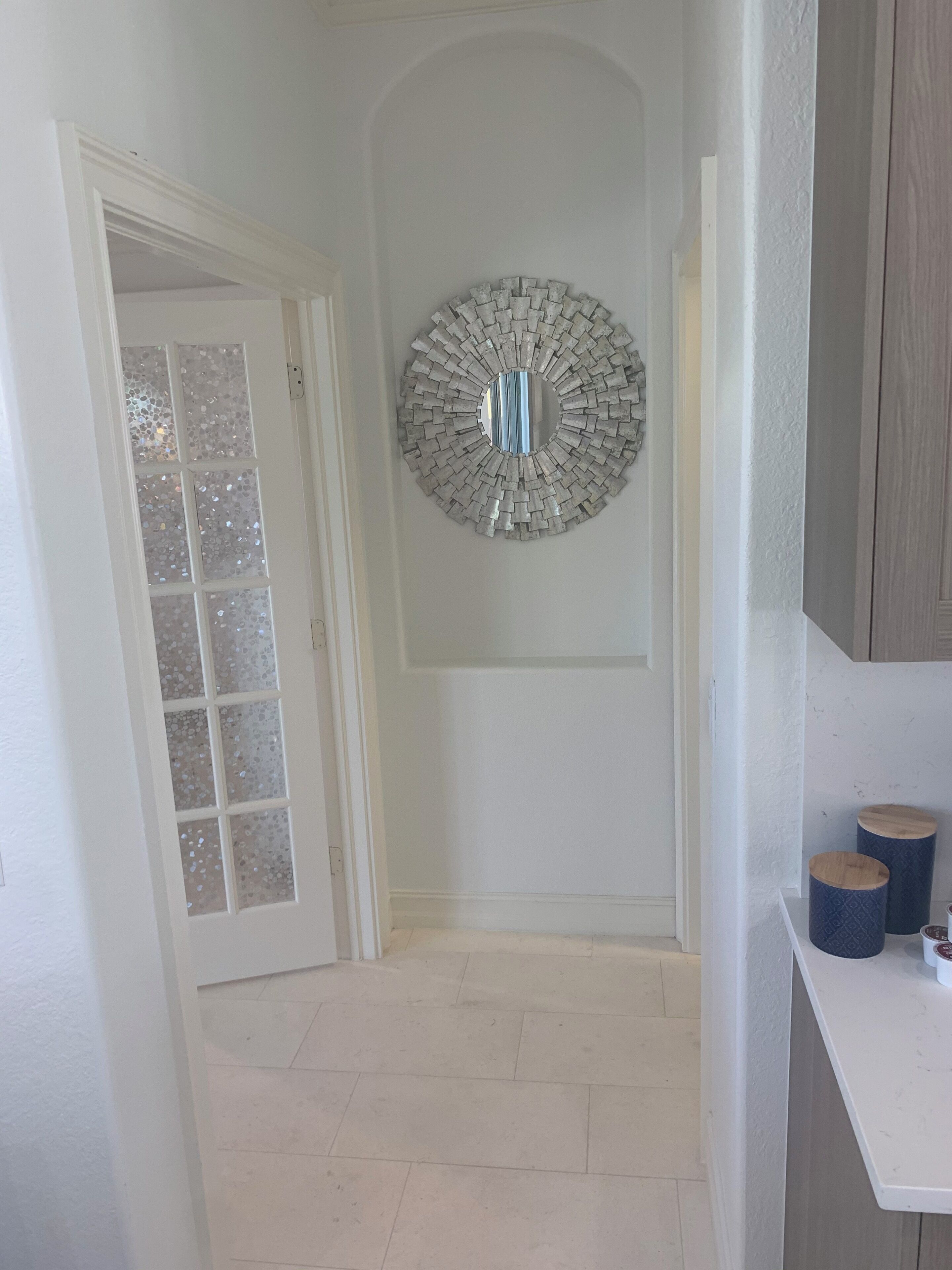 A hallway with a white door, a decorative mirror, and a white counter with two cylindrical containers.