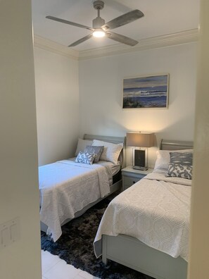 A bedroom with two single beds, a ceiling fan, a nightstand with a lamp, and a painting on the wall. - Island Time Starts Here! 3BR + Den Pool Retreat (Marco Island)