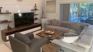 A modern living room with a flat-screen TV, a sofa, a coffee table, and a large window. - Island Time Starts Here! 3BR + Den Pool Retreat (Marco Island)