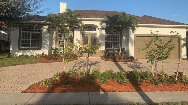 A two-story house with a garage, a front porch, and a landscaped garden with small trees and shrubs. - Island Time Starts Here! 3BR + Den Pool Retreat (Marco Island)