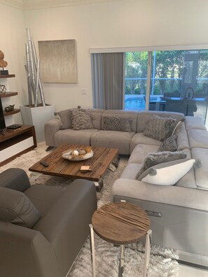 A modern living room with a sectional sofa, a coffee table, and a small side table. - Island Time Starts Here! 3BR + Den Pool Retreat (Marco Island)