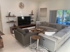 Ein modernes Wohnzimmer mit Fernseher, grauen Sofas, einem Couchtisch und Dekorationen auf Regalen.