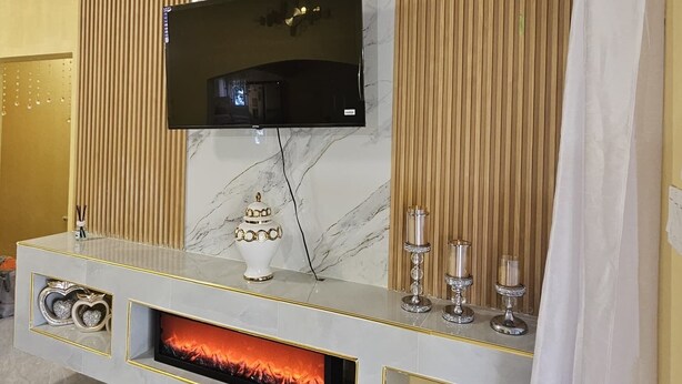 A modern living room with a flat-screen TV mounted on a marble wall, a fireplace with a glass front, and decorative items on the mantel. - 2-bedroom house in wonderful Golden Grove with air conditioning (Golden Grove)