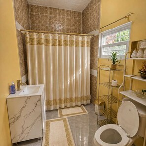 Un baño con tocador de mármol, inodoro, cortina de ducha y una ventana con una planta.
