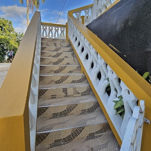 Eine Treppe mit einem fußbodenähnlichen Fliesenmuster, einem weißen Geländer und einem gelben Handlauf.