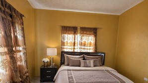 A bedroom with a large bed, a nightstand with a lamp, and curtains. - 2-bedroom house in wonderful Golden Grove with air conditioning (Golden Grove)