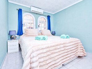 A bedroom with a bed, two windows, a nightstand, a lamp, and a wall-mounted air conditioner. - Oasis 10 by Interhome (El Carmoli)