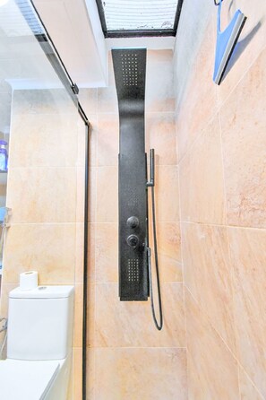 A shower with a handheld showerhead and a wall-mounted control panel in a bathroom with beige tiles. - Oasis 10 by Interhome (El Carmoli)