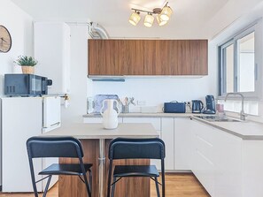 A modern kitchen with white cabinetry, a wooden countertop, two black chairs, a white vase, and a built-in microwave. - Le Grand Large by Interhome (Le Lavandou)
