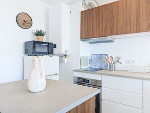 Una cucina moderna con mobili bianchi, un forno a microonde, un bollitore e un vaso sul piano di lavoro.