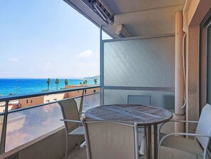 En balkon med et bord og stole, der kigger ud over en strand med palmer og havet.