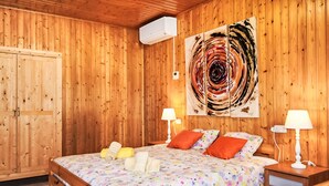 Quarto com painéis de madeira, uma cama, duas luminárias de apoio e um grande quadro abstrato.