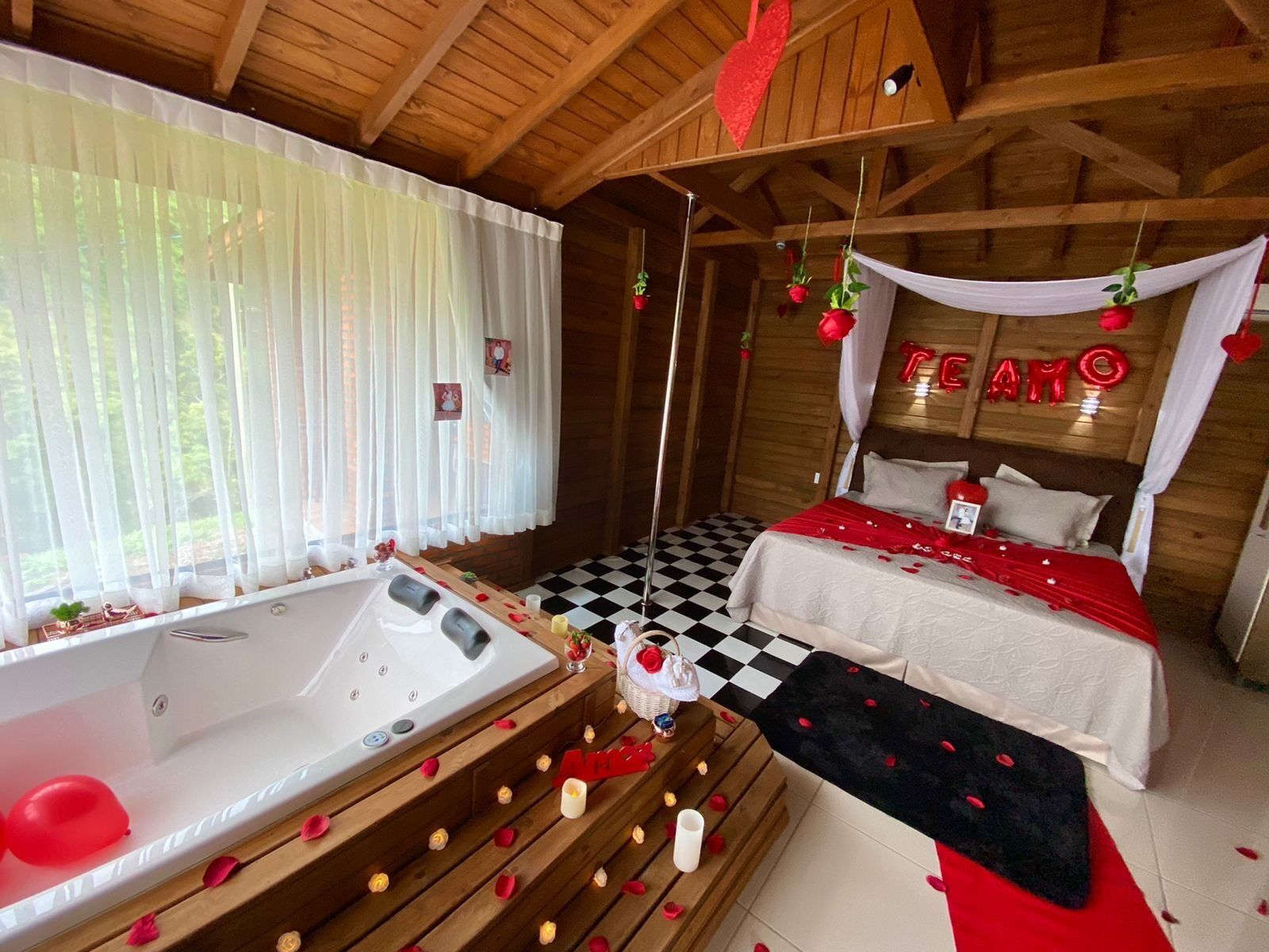 Una habitació acollidora amb un terra de pissos de graella, un llit amb roba de llit vermella i blanca, una banyera i un llit amb cortina on es llegeix 'LOVE'.