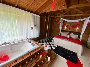 Ein gemütliches Zimmer mit kariertem Boden, einem Bett mit rot-weißer Bettwäsche, einer Badewanne und einem Himmelbett, an der Wand ist 'LOVE' geschrieben.