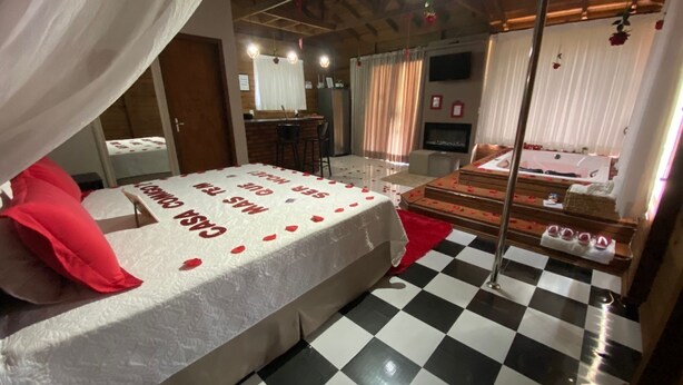 Une chambre d’hôtel avec un sol à carreaux, un lit à baldaquin, un coin salon avec une table et des chaises, et une vue sur l’espace piscine.