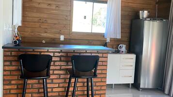 Una cocina con una isla de ladrillo, dos taburetes de bar, un refrigerador y lámparas colgantes.