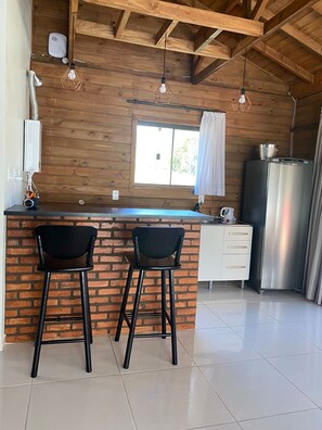 A kitchen with a brick island, two bar stools, a refrigerator, and hanging pendant lights. - Cabin of Two Loves. Romantic destination. (São Leonardo)