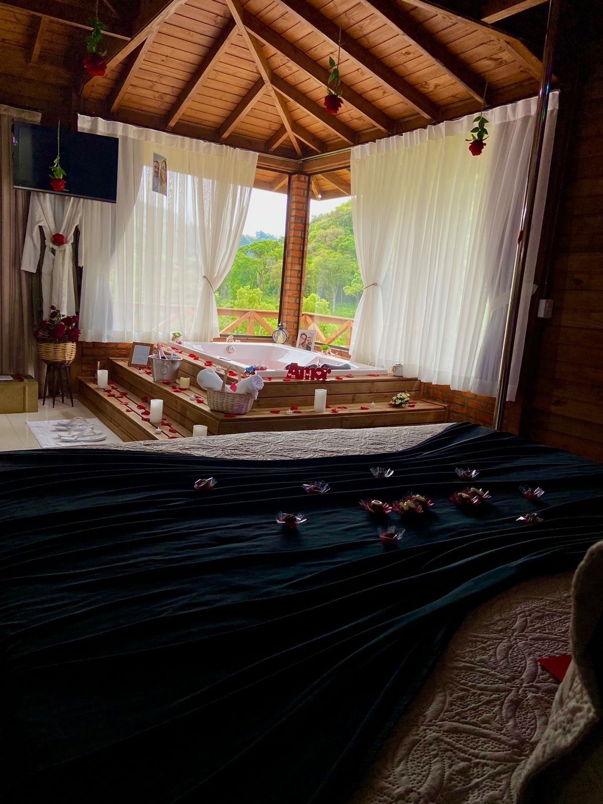 A cozy room with a wooden ceiling, a large bed with a dark blue bedspread, and a view of greenery outside.