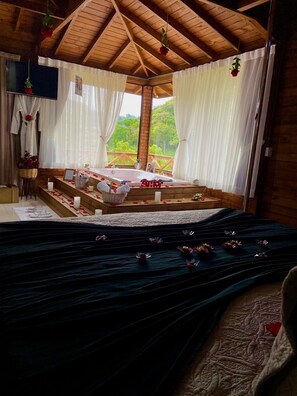 A cozy room with a wooden ceiling, a large bed with a dark blue bedspread, and a view of greenery outside.