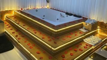 Un área de spa con un jacuzzi grande, escalones de madera y pétalos de rosa.