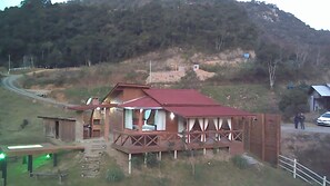 A rustic cabin with a red roof, a porch with curtains, and a dirt path leading to the entrance.