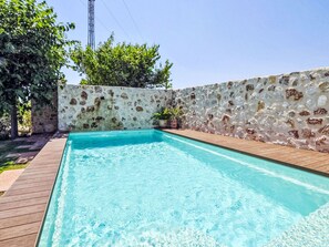 A rectangular swimming pool with a wooden deck surrounding it, set against a stone wall with some greenery and a power line in the background. - Hort des Padri by Interhome (Marratxi)