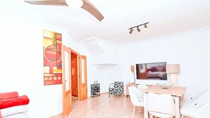 A modern living room with a flat-screen TV, a dining area with a table and chairs, and a ceiling fan. - Olivos 3 by Interhome (Los Urrutias)