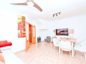 A modern living room with a flat-screen TV, a dining area with a table and chairs, and a ceiling fan. - Olivos 3 by Interhome (Los Urrutias)