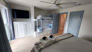 Ein Schlafzimmer mit einem Bett, einem Deckenventilator, einem an der Wand montierten Fernseher und einem Kleiderschrank mit integriertem Regal.